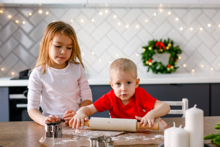 A 6-year-old girl and a 2-year-old boy are rolling out dough in the kitchen, embracing the Christmas spirit.の写真素材