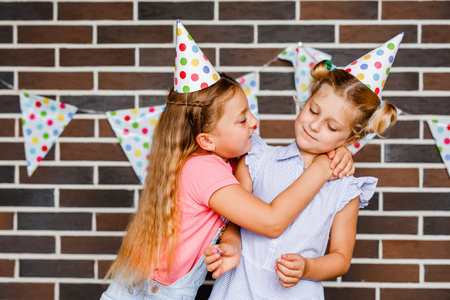 Two girls in holiday hats hugging and saying happy holidays.