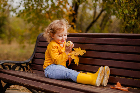 Joyful toddler girl with curls in a yellow shirt in fall park.の写真素材
