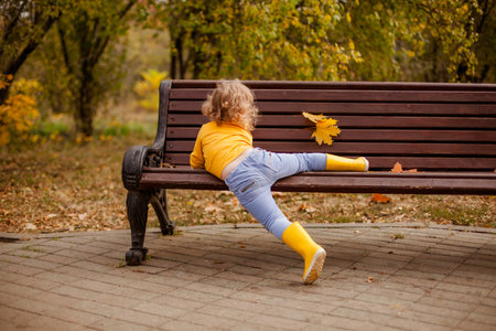 Toddler girl with curly hair in a yellow shirt playing in an autumn park.の写真素材