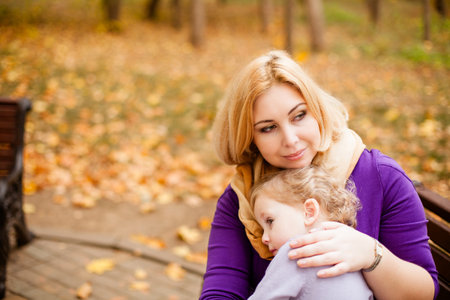 Loving mother in purple dress hugging her sad daughter on park bench.の写真素材