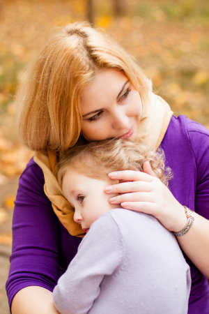 Plus-size woman in purple dress gently hugging her crying 3-year-old daughter on a bench in an autumn park.の写真素材
