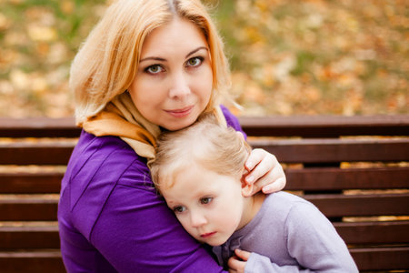 Loving mother in purple dress hugging her sad daughter on park bench.の写真素材