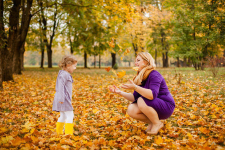 Plus-size woman in purple dress holding and playing with her 3-year-old daughter in autumn park.の写真素材