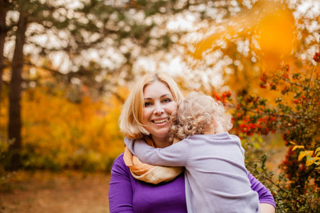 Loving mother in purple dress hugging her sad daughter on park bench.の写真素材