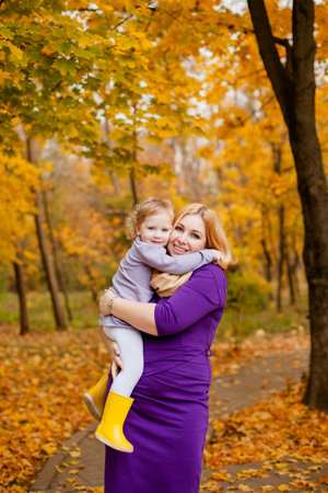 Plus-size woman in purple dress holding and playing with her 3-year-old daughter in autumn park.の写真素材