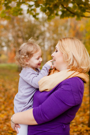Plus-size woman in purple dress holding and playing with her 3-year-old daughter in autumn park.の写真素材