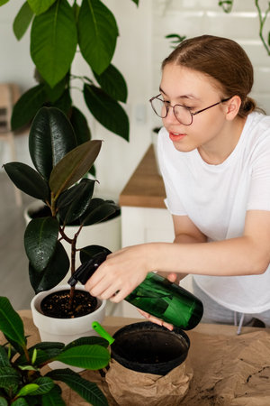 Young slim woman in white t-shirt watering houseplants in stylish living roomの写真素材