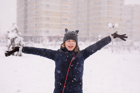 Portrait of a 12-year-old girl in a warm jacket and a cat-ear hat under heavy snow.の写真素材