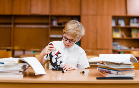 Boy in glasses carefully studying textbooks at a school desk.の写真素材