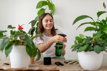 Young slim woman in white t-shirt watering houseplants in stylish living roomの写真素材