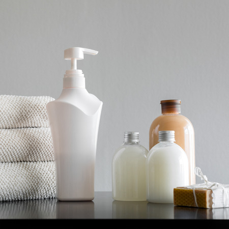 Pile of towels with shampoo, body lotion, shower milk and handmade soap on neutral background.の写真素材