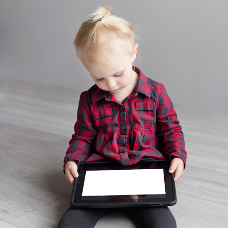 Little cute girl holding a tablet and looking at him. Mock upの写真素材