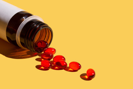 Red jelly capsules with vitamin E, poured from a bottle on a yellow background