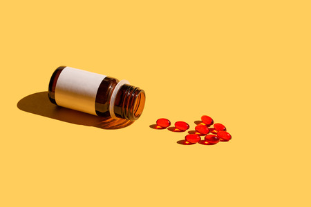 Pills spilling out of pill bottle forming an arrow sign on yellow background.の写真素材
