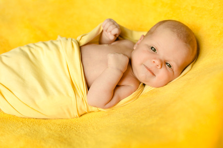 A cute newborn baby lies on a yellow blanket wrapped in a yellow plaid and smilingの写真素材