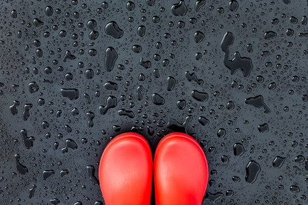 The edges of the red rubber boots are on a wet wet surface covered with raindrops. Copy space. Top view.の写真素材