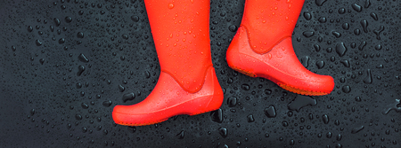 The edges of the orange rain boots are on a wet wet surface covered with raindrops. Top view, copy space.の写真素材