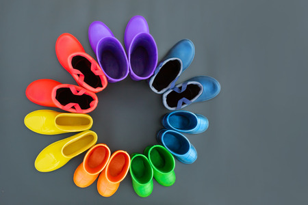 Colorful rubber boots of all colors of the rainbow-red, orange, yellow, green, blue, cyan and purple stand on the gray surface in a circle. Top view, space for text.の写真素材