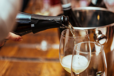 Champagne is poured into a glass standing on the table. Close up.の写真素材