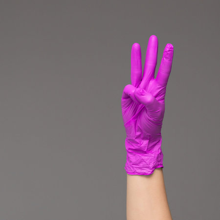 hand in surgical glove shows three fingers on neutral background. Copy space.