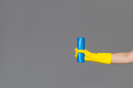 Hand in rubber glove holds blue garbage bag on neutral background. The concept of spring cleaning.の写真素材