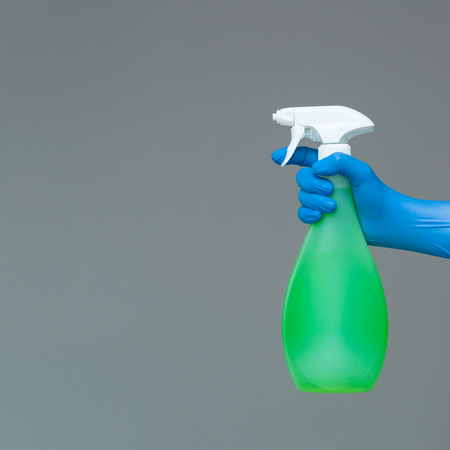 A hand in a rubber glove holds the glass cleaner in a spray bottle on a neutral background. The concept of bright spring, spring cleaning.の写真素材