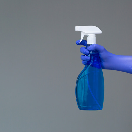 A hand in a rubber glove holds the glass cleaner in a spray bottle on a neutral background. The concept of bright spring, spring cleaning.の写真素材
