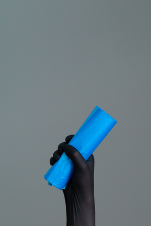 Hand in rubber glove holds colored garbage bag on neutral background. The concept of bright spring, spring cleaning.の写真素材