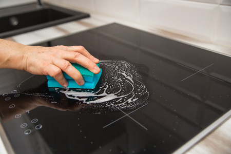 A woman's hand with a blue sponge rubs a glass ceramic plate in the kitchen.の写真素材
