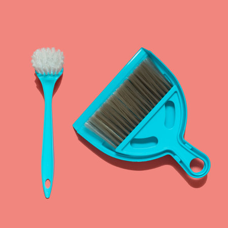 A pale blue dustpan, brush and brush for dish washing lying on living coral background. In the style...