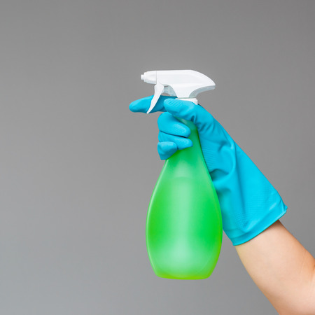 A hand in blue rubber glove holds the glass cleaner in a spray bottle on a neutral background. The concept of bright spring, spring cleaning.の写真素材