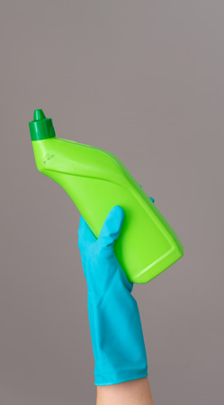 A hand in a rubber glove holds a bottle of plumbing detergent on a neutral background. The concept of bright spring, spring cleaning.の写真素材