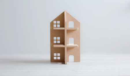 Toy wooden house on white wooden floor and bright background. Symbol of family, new estates and development.の写真素材
