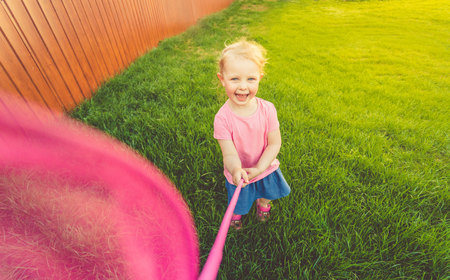A little cute girl in a pink t-shirt and denim skirt runs around the field and catches butterflies. Close up. Lifestyle. Toned.の写真素材