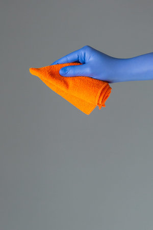A hand in a rubber glove holds a bright microfiber duster on a neutral background. Ð¡oncept of...