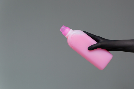 A hand in a rubber glove holds a bottle of plumbing detergent on a neutral background. The concept of bright spring, spring cleaning.の写真素材