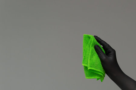 A hand in a rubber glove holds a bright microfiber duster on a neutral background. Ð¡oncept of...