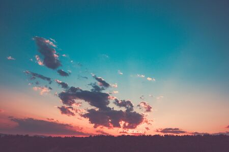 Stunning living coral sunset over the forest with clouds and breaking through the rays of the sun.の写真素材