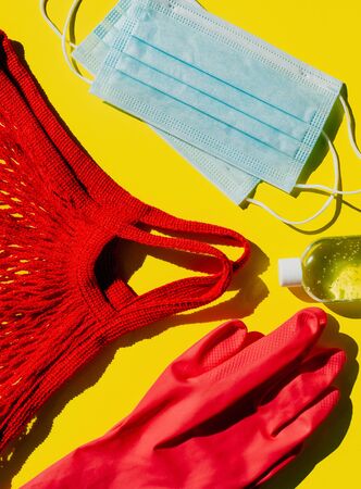 Covid personal protection kit - 19 visits to shops and other public places during the pandemic. Antiseptic, face masks, gloves and string bag on a yellow background.の写真素材