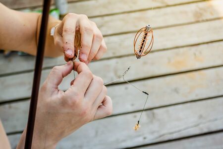 Close-up of the hands of a fisherman who impales worms on the hook of a fishing rod on a wooden pier.の写真素材