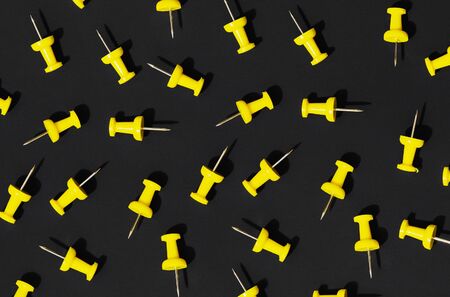 A pattern of scattered yellow office pushpins on a black background. Hard light, shadows.の写真素材