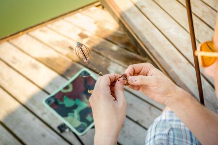 Close-up of the hands of a fisherman who impales worms on the hook of a fishing rod on a wooden pier.の写真素材