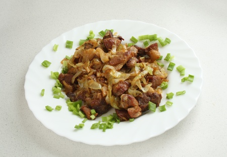fried cabbage with fried pork meat on a white plate with green chopped onionの写真素材