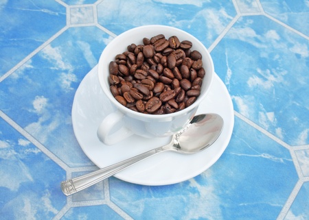cup of coffe beans with a spoon on blue backgroundの写真素材