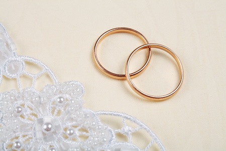 Pair of golden wedding rings over invitation card decorated with laceの写真素材