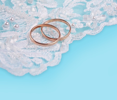 Pair of golden wedding rings over invitation card decorated with laceの写真素材