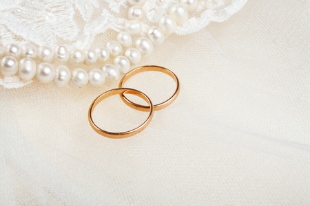 Pair of golden wedding rings over invitation card decorated with laceの写真素材