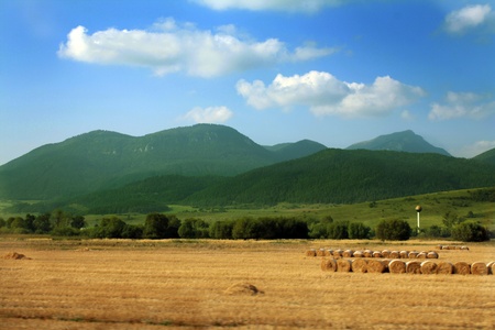 Beautiful countryside landscape. Round straw bales in harvested fields, mountains and blue sky with clouds の写真素材