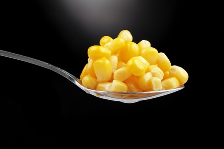 spoon with sweet corn over black background with vapor under itの写真素材